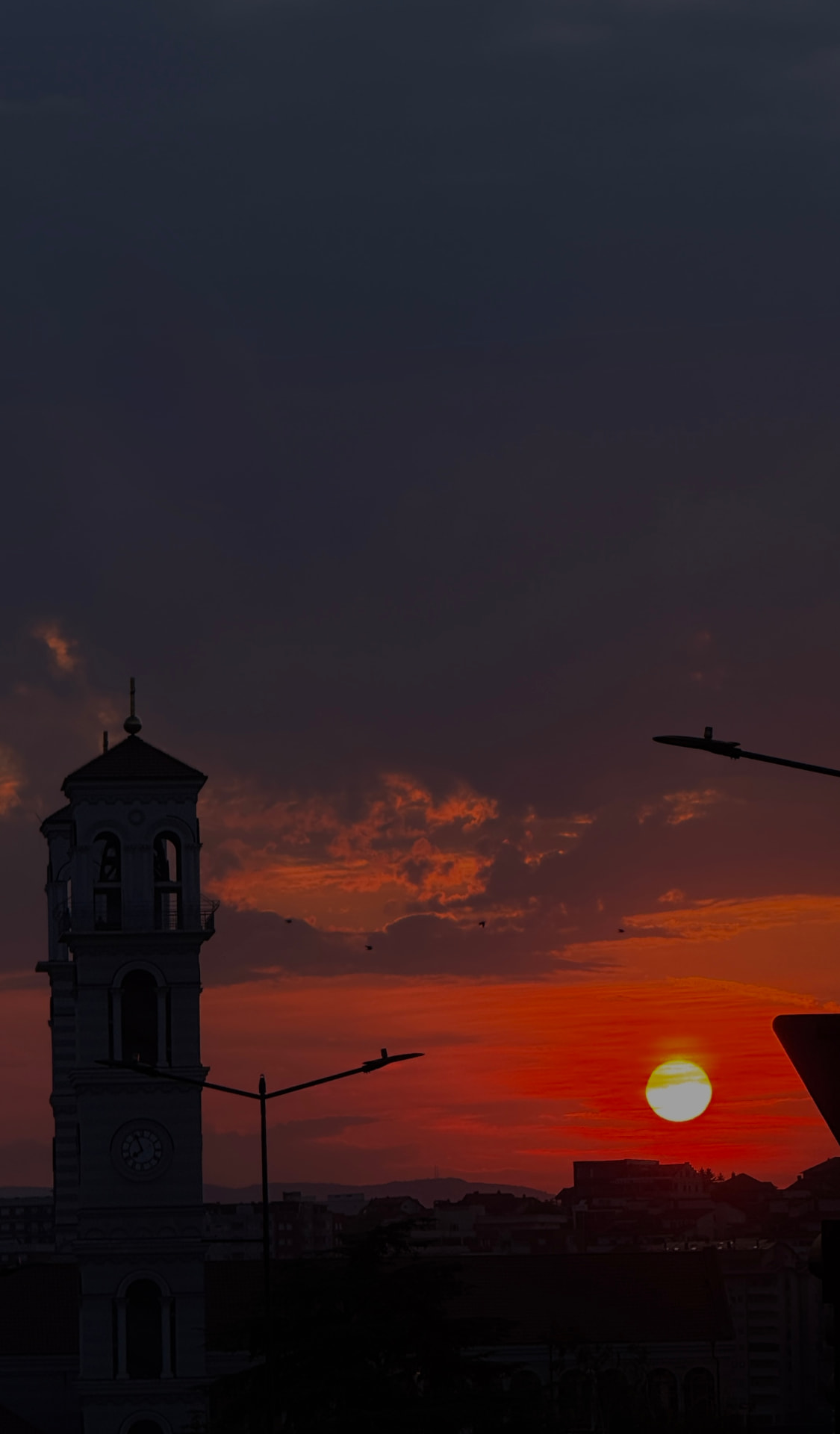Clock tower silhouetted against a red sunset over Prishtina, Kosovo