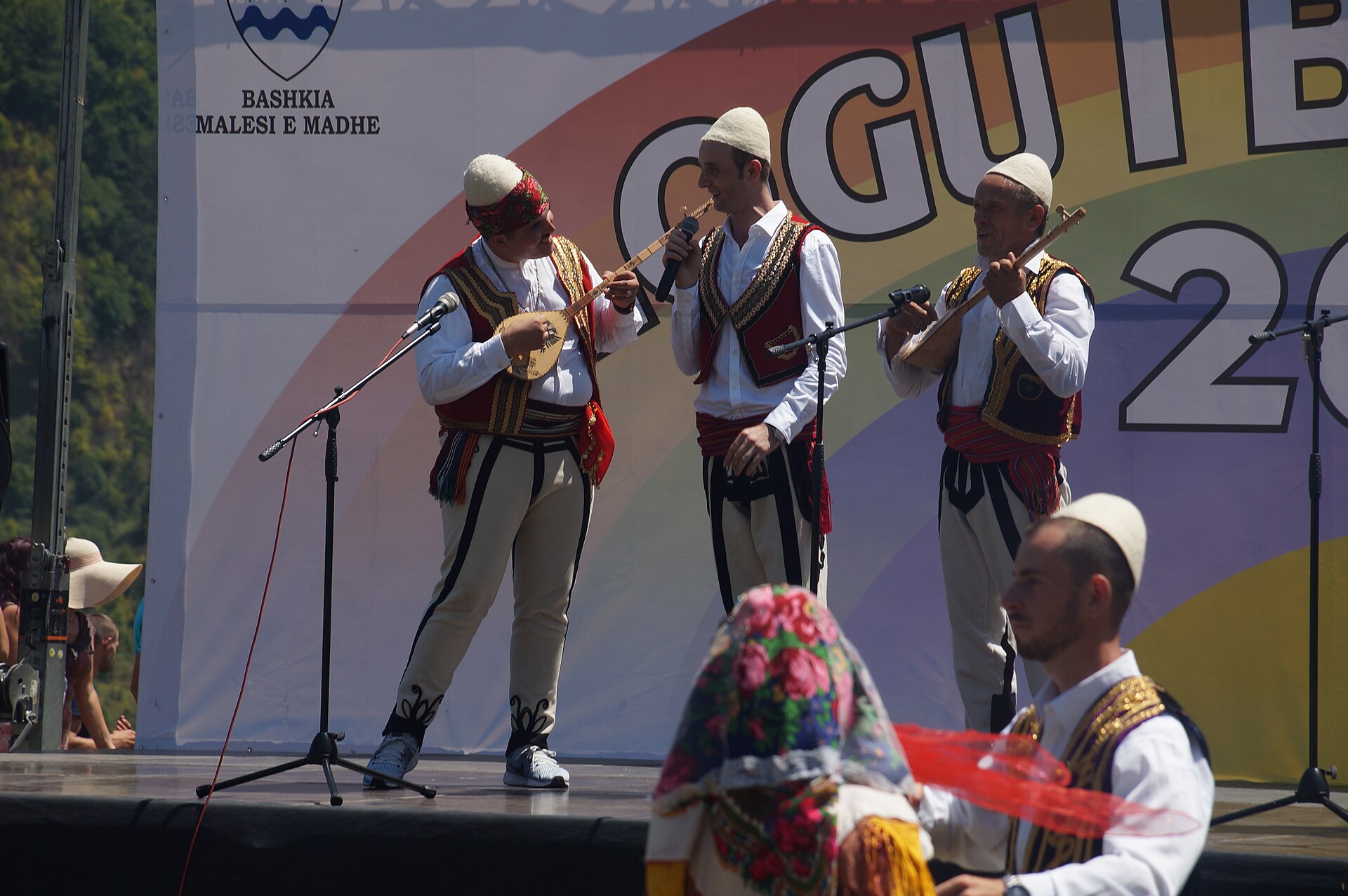 Musicians in traditional Albanian dress playing folk instruments at an outdoor cultural gathering in the Kosovo highlands